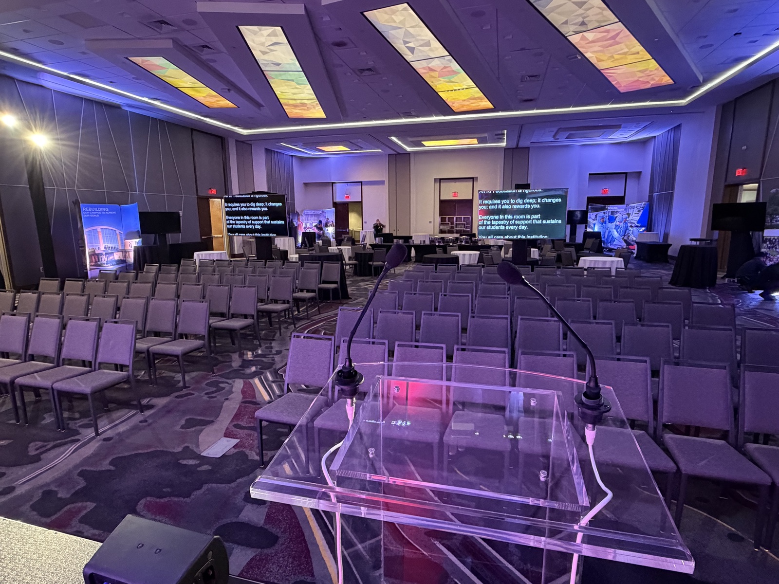 Acrylic podium with gooseneck mics facing confidence monitors in a ballroom